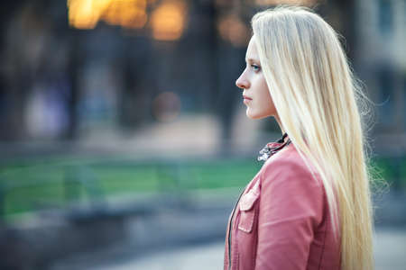 Profile portrait of young beautiful blond woman in city street on sunset with copy spaceの写真素材