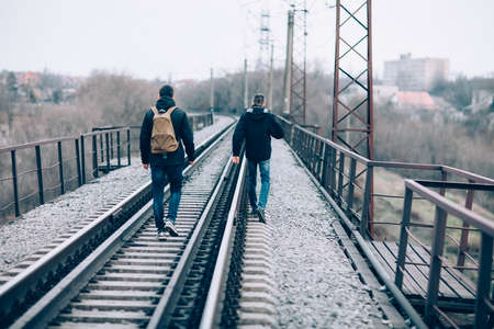 Back view of two men walking away on the railroad tracksの写真素材