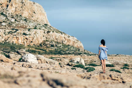 Back view of lonely woman walking on rocky desert with dramatic skyの写真素材