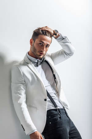 Portrait of handsome stylish man in white elegant suit leaning at wall