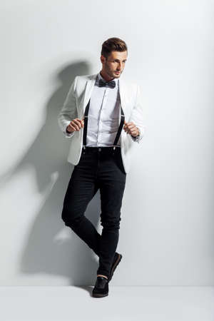 Full length portrait of handsome stylish man in white elegant suit posing and leaning at wallの写真素材