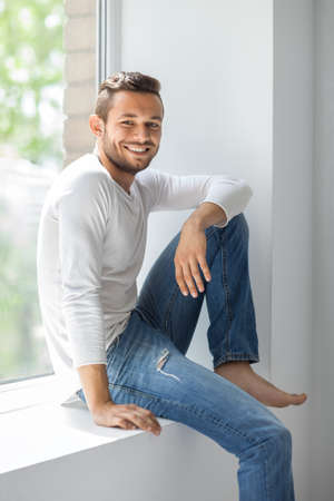 Happy smiling man relaxing on window sill. wellbeing conceptの写真素材