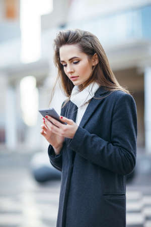Pretty young woman on the city street with mobile phone writing smsの写真素材