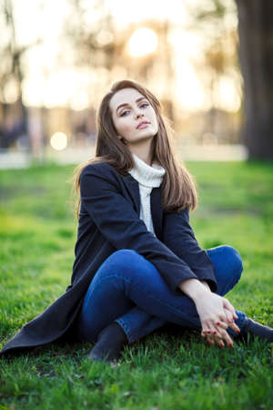 Young beautiful woman sitting on a grass in sun light on sunset time. Relax concept
の写真素材