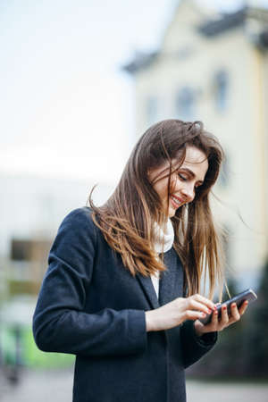 Happy beautiful woman on the city street with mobile phone writing smsの写真素材
