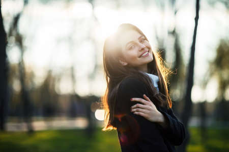Smiling beautiful woman portrait in sun light on sunset time in city parkの写真素材