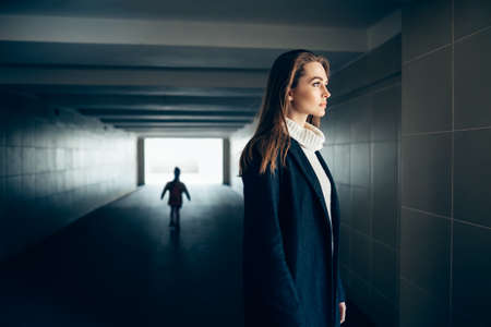 Beautiful lonely woman in a subway tunnel with frighten silhouette on background. surrealism conceptの写真素材