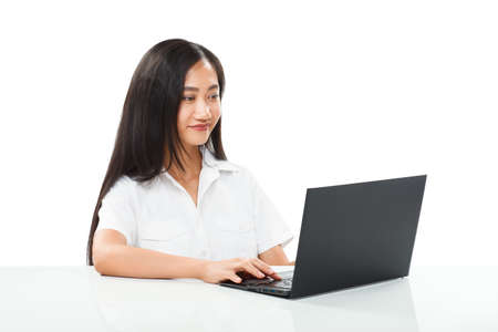 Young pretty smiling Asian woman typing on black laptop and looking at camera. Manager, office worker or student female model. Half body portrait isolated on white backgroundの写真素材