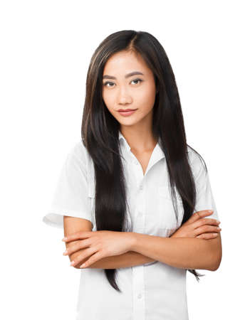 Portrait of beautiful Asian young woman in white shirt with long brunette hair and crossed arms on chest. Model looking at camera and light smiling. Photo isolated on white backgroundの写真素材