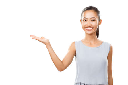 Studio portrait of Asian cheerful woman with open palm showing or presenting abstract product. Young female model happy smiling and looking at camera. Brunette girl in elegant casual clothes isolated on white backgroundの写真素材