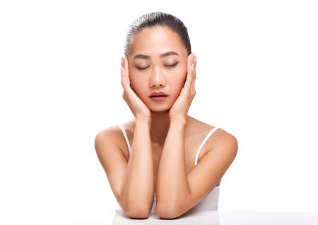 Beautiful young Asian woman with closed eyes and calm face. Girl sitting and bent head on her arm. Model with oriental appearance and light make-up. Closeup portrait isolated on white backgroundの写真素材