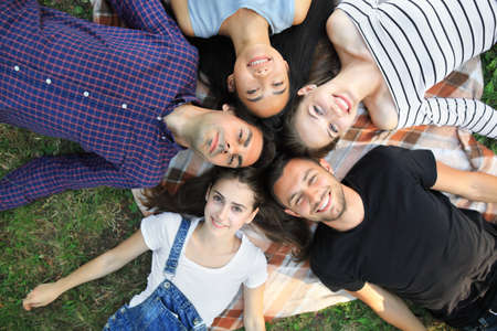 Five cheerful friends lying on grass top view portrait. Happy young women and men in casual clothes having fun outdoors. Male and female models looking at camera and smilingの写真素材