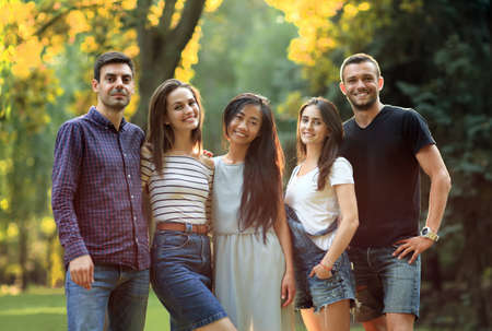 Five young people friends looking at camera in sunny park. Beautiful men and women company walking together in free weekend. Team, friendship, unity conceptの写真素材