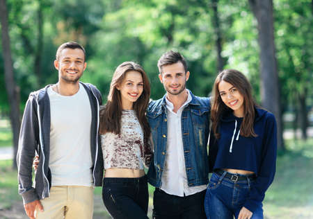 Four young cheerful friends are walking on warm day. Two Caucasian men and two women having fun together outdoors. Half body portrait of smiling people. Models looking at cameraの写真素材