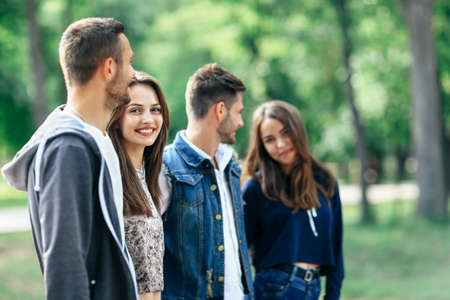 Happy young couples spend fun time. Focus on beautiful woman with long hair, she smiling and looking at camera. Half body portrait of people on green trees blur background. Love and friendship conceptの写真素材
