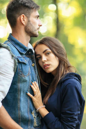 Young beautiful woman embracing her man outdoors. Girl looking at camera. Caucasian couple of lovers in park on green trees background. Trust, support, relationship of two peopleの写真素材