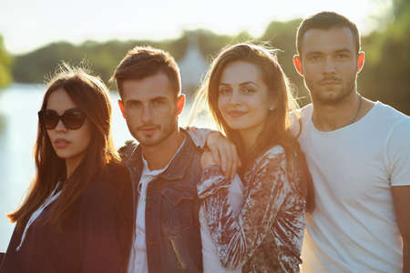 Two women and men on river background on sunny day. Happy people standing close to each other in row, smiling and looking at camera or in the distance. Image with lens flare effectの写真素材