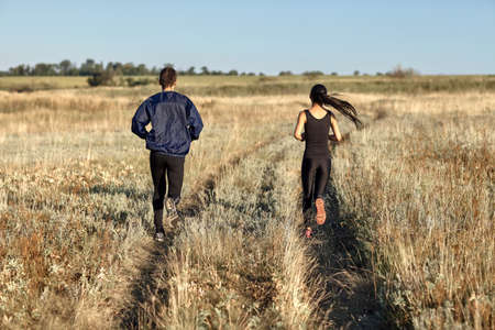 Woman and man training in field, jogging back view. Two young athletic people running in countryside on sunny day. Healthy lifestyle, sport, motivation, team concept. Photo with copy spaceの写真素材