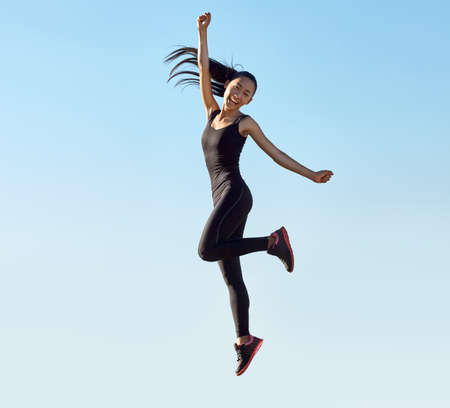 Young sporty asian woman jumping high like superhero. Full-length portrait in motion. Positive emotions, success conceptの写真素材
