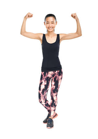 Slim happy Asian woman showing muscles on hands biceps. Fitness sportswoman wearing training suit, smiling and looking at camera. Healthy lifestyle, strength health concept. Portrait isolated on whiteの写真素材