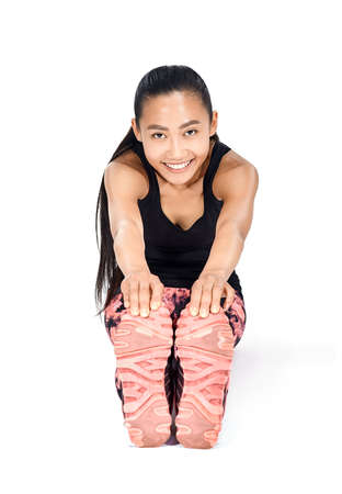 Young beautiful Asian woman doing stretching body and legs sitting. Happy healthy female athlete warming up for training. Sport girl smiling and looking at camera. Portrait isolated on whiteの写真素材