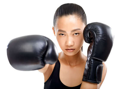 Portrait of Asian woman wearing boxing clothes, focus on gloves. Young serious athlete girl and boxing gloves are blurred. Photo isolated on white backgroundの写真素材