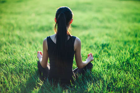 Sports fitness woman meditating on grass, back view. Young Asian woman practicing meditation on grass. Quiet rest after sportsの写真素材