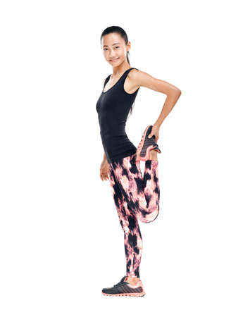 Sporty young Asian woman doing stretching legs. Full-length isolated portrait of fitness girl warming up before workout. Photo in profile of slender model in tracksuitの写真素材