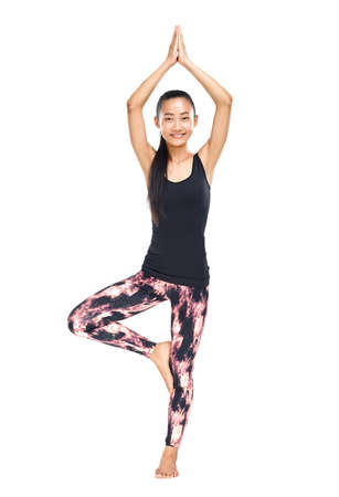 Athletic Asian woman standing in yoga pose tree Vrikshasana isolated. Young girl exercising and making asana. Female model practicing yoga or gymnastics. Harmony, meditation, healthy lifestyle conceptの写真素材