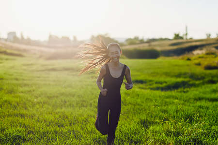 Chinese woman in black sports overalls runs camera in sunshine. Young girl runs to meet in the sun and smiles, enjoys life, rejoices. Image with lens flare effectの写真素材