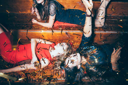 Beautiful young women having fun on crazy party lying on the floor in confetti. New year, Birthday, Holiday Event Conceptの写真素材