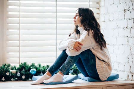 Young beautiful woman relaxing on window sill in christmas decorated home. Holiday conceptの写真素材