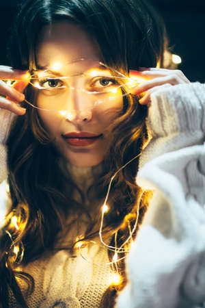 Close up portrait of a beautiful young woman with christmas lights. Holiday concept