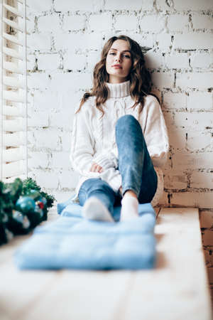 Young beautiful woman relaxing on window sill in christmas decorated home. Holiday conceptの写真素材
