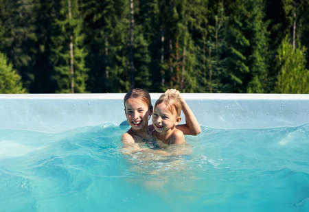 Portrait of brother and sister fooling around in outdoor pool. Children frolic in pool against...