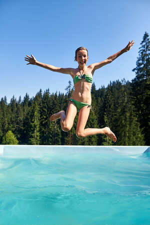 Teenager girl falls into swimming pool outdoor and shouts. Schoolgirl enjoys vacation in nature. Sanatorium surrounded by pristine forest nature. Active leisure in open air and scenic landscapeの写真素材