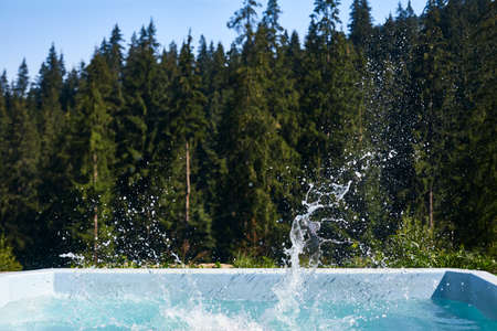 Pool with splashes in air on background of coniferous forest. Place for swimming outdoors with picturesque view. Holiday, vacation, weekend, entertainment conceptの写真素材