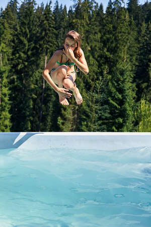 Girl jumps into swimming pool, holding nose. Children outdoors dive into water. Active leisure in nature and picturesque scenic landscapeの写真素材