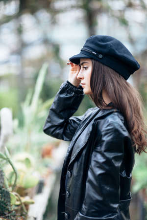 Profile portrait of young fashion woman in leather jacket and cap on nature backgroundの写真素材