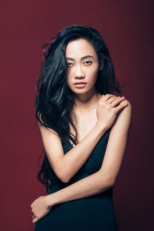 Beautiful asian woman in black dress posing in studio on brown background. Pretty fashion model portraitの写真素材