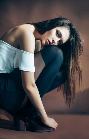 Young attractive woman posing on brown background sitting on squat, head on knees. Lonely conceptの写真素材