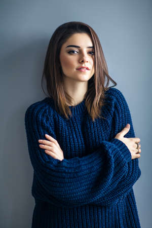 Portrait of young sensual woman with crossed arms posing on gray backgroundの写真素材