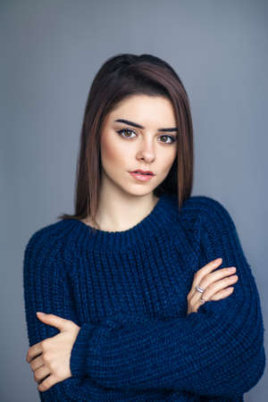 Portrait of young sensual woman with crossed arms posing on gray background