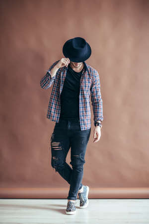 Full length portrait of a handsome man touching his hat posing on brown background. Danceの写真素材