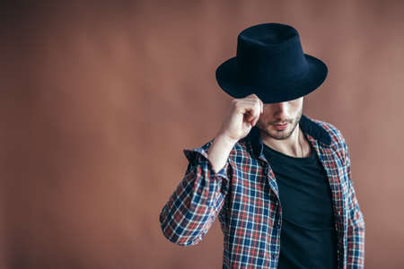 Young hipster man wearing hat posing on brown background with copy spaceの写真素材