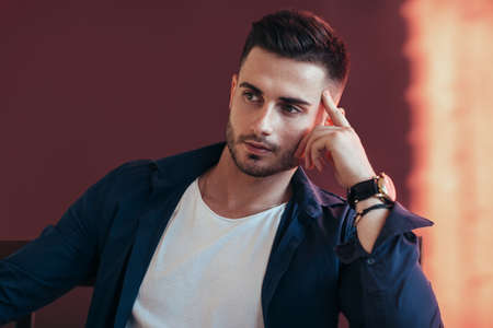 Handsome thoughtful man on dark red background. の写真素材