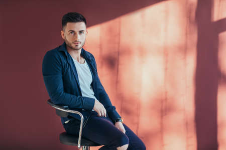 Portrait of confident and handsome man sitting on chair with copy space on red wall srudio background の写真素材