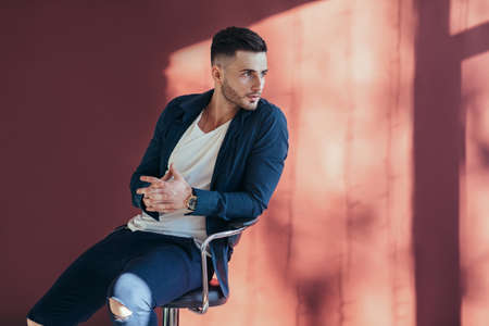Portrait of confident and handsome man sitting on chair with copy space on red wall srudio background の写真素材