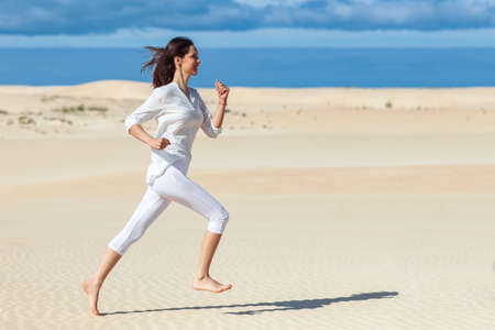 Beautiful girl in sportswear running in desert. Side view of active athletic young woman running on sand. Photo with copy spaceの写真素材