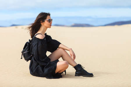 Beautiful young woman in long black dress posing in desert, Spain. Girl relax and enjoying summer...